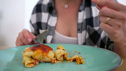 Person in checkered shirt cutting into a serving of homemade enchiladas on a green plate, ready to enjoy a tasty meal