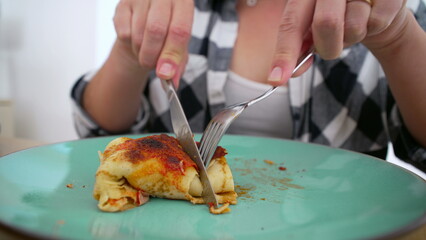 Person in checkered shirt cutting into a serving of homemade enchiladas on a green plate, ready to enjoy a tasty meal