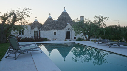 Relaxing poolside scene in alberobello, italy, showcasing traditional trulli houses, olive trees,...