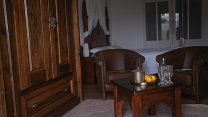 Interior of a cozy room with wooden furniture, leather armchairs, citrus fruits on a table, and crystal glasses