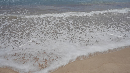 A tranquil beach with foamy waves gently lapping against the sandy shore under a clear sky.