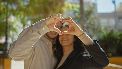 A loving couple forms a heart with their hands in a sunny park, embodying romance and togetherness in nature.