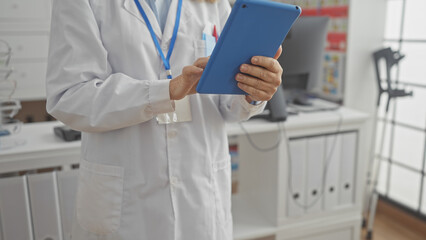 A woman pharmacist in a white coat uses a tablet in a modern pharmacy