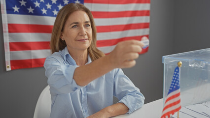 A middle-aged woman smiling while voting in an american election with a ballot and flag in the...