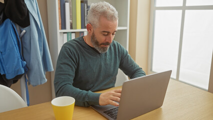 A mature man with grey hair working on a laptop in a home setting, exuding casual professionalism.