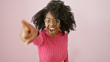 Joyful african woman pointing smiling indoors with glasses and curly hair.