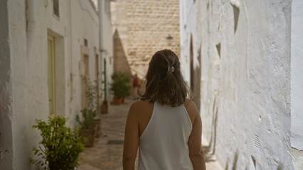 A young hispanic woman walks down the charming whitewashed streets of locorotondo, in the old town of puglia, italy, capturing the essence of european beauty and tranquility.
