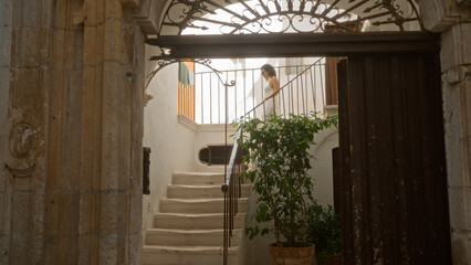 Obraz premium A young hispanic woman walks up white stairs in the charming old town streets of locorotondo, puglia, italy, surrounded by rustic architecture and greenery.