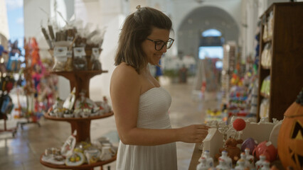 Young hispanic woman shopping in the charming streets of gallipoli, puglia, italy, exploring local markets and admiring beautiful handmade crafts.