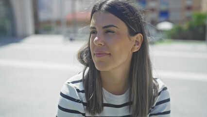 A beautiful hispanic brunette woman enjoying the urban outdoors on a sunny day in the city, wearing a black and white striped shirt.