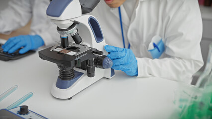 Two male scientists collaborate using a microscope in a laboratory setting, implying medical research and teamwork.