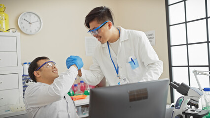 Two men handshake in a laboratory setting, portraying a sense of teamwork and scientific collaboration.