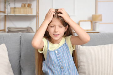 Little girl with pediculosis scratching her head on sofa at home