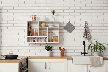 Glass jars with different products and condiments on shelves in kitchen