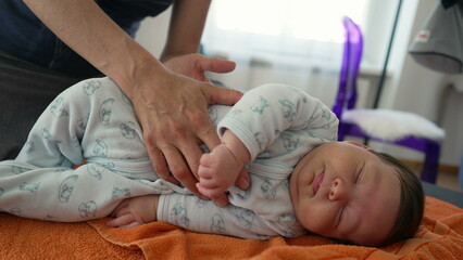 Orthopedist adjusting newborn's position on an orange towel to relieve body pains during early childhood, baby is in a cozy onesie, showing the careful and professional approach
