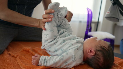Orthopedist adjusting newborn's position on an orange towel to relieve body pains during early childhood, baby is in a cozy onesie, showing the careful and professional approach