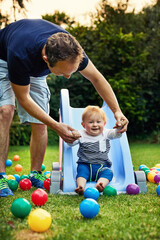 Outdoor, dad and playing with baby, slide and bonding with child, toys and smile for fun and family. Backyard, cute toddler and games with father, love and playground with ball, man and parent