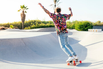 back view of unrecognizable funky young male skateboarder in trendy colorful shirt and jeans...