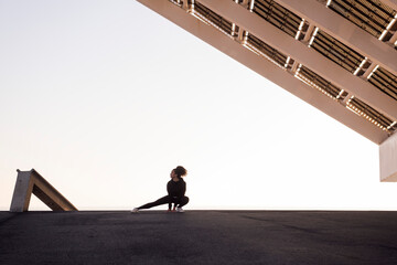 Fototapeta premium african american female athlete performing side squat during training under modern house while looking away in city, concept of urban sports and healthy lifestyle
