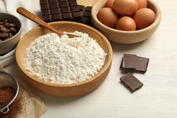 Flour in bowl and chocolate for making dough on light wooden table, closeup