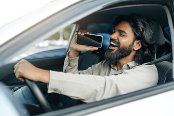 Smiling middle eastern man with long hair and a beard enthusiastically sings while holding his...