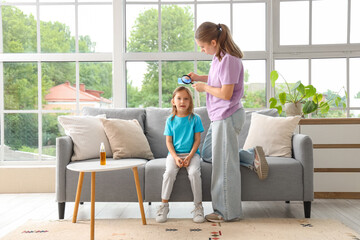Mother with magnifier combing her little daughter's hair with pediculosis at home