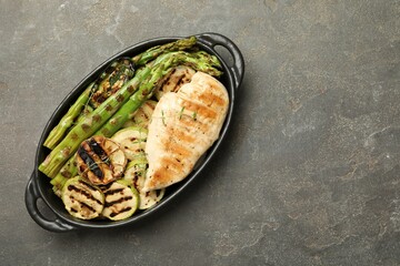 Delicious grilled vegetables and chicken breast in baking dish on grey table, top view. Space for text