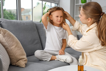 Mother checking her little daughter's hair with pediculosis on sofa at home