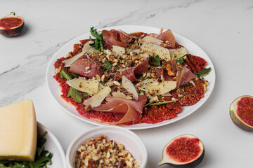 Close-up of appetizing appetizer carpaccio of figs, prosciutto, arugula and parmesan sprinkled with walnuts on a plate
