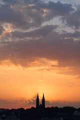 Fototapeta premium Morning sun rising among two church towers. Beautiful cozy sunrise over the city.