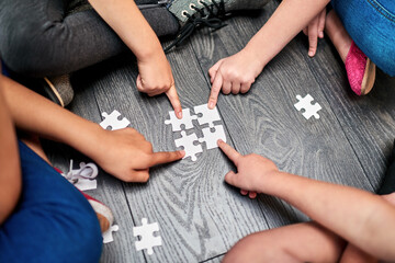 Above, kids and hands with puzzle for playing, cognitive development and solution skills by floor. Teamwork, children and solidarity with jigsaw for problem solving, support and friends for bonding
