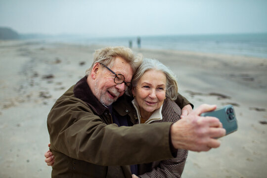 Smiling senior couple taking a selfie on beach during winter