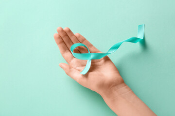 Female hand with light blue ribbon on turquoise background. World Cancer Day