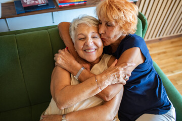 Happy senior lesbian couple embracing and smiling at home on couch