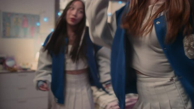 Two long-haired teenage girl friends in bomber jackets dancing to k-pop song in bedroom