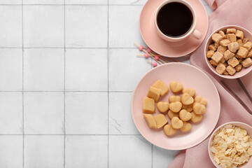 Plate with tasty marzipan candies, almond flakes, sugar and cup of coffee on white tile background