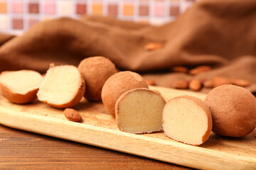 Board with tasty marzipan candies covered with cocoa powder on wooden table, closeup