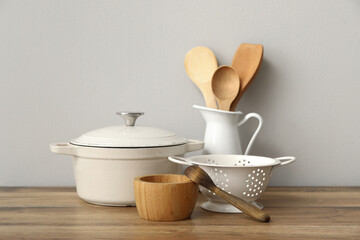 Cooking pot, colander and wooden utensils on table near white wall