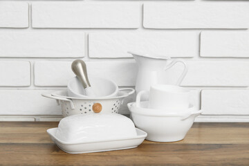 Different porcelain dishes on wooden table near white brick wall