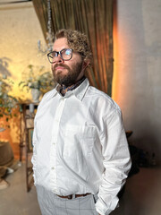 Thoughtful man in a white shirt stands confidently in a warmly lit room with a classic and elegant background interior. Confidence, elegance and male fashion concept