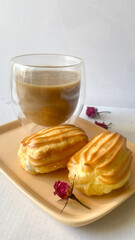 A cup of coffee and eclairs, a plate of profiteroles on a light gray marble background, a delicious breakfast.