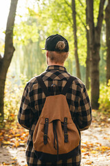 Traveler with a backpack is walking on an road along autumn forest.