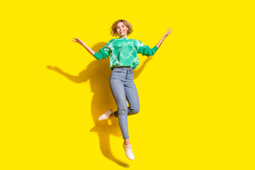 Full length photo of adorable lovely girl wear tie dye sweatshirt jumping high empty space isolated yellow color background