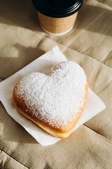 Paper cup of coffee and heart-shaped donut on a napkin, close-up.