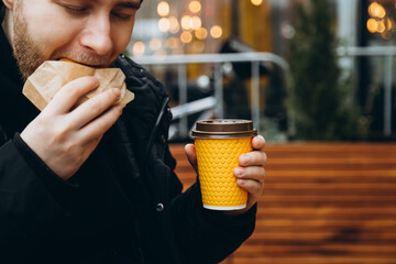 Bearded man eating a burger on a blurred background with bokeh outside.