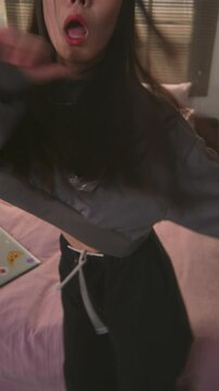 Vertical view of Korean girl in casual clothes looking at camera while dancing k-pop and lip syncing in her room
