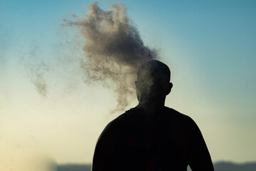 Silhouetted man is seen smoking an e-cigarette outdoors on a sunny day during sunset in the city of...
