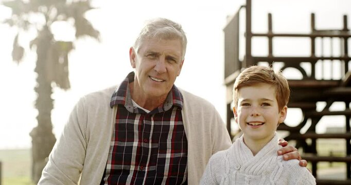 Happy grandfather and grandson bonding together on a seaside promenade. Portrait of a cheerful young boy and senior man together outside during summer while enjoying a family outing at the park