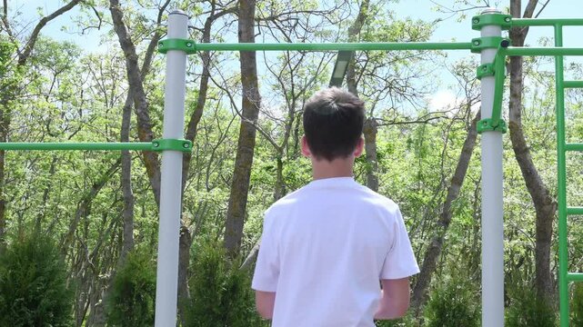 thin teenager, a schoolboy of 14 years old, plays sports on the playground, pulls himself up, does a warm-up. High quality 4k footage
