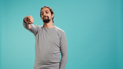 Upset man showing thumbs down sign gesturing, being disapproving. Disappointed Arab person against gaming, doing rejection hand gesture, isolated over studio background, camera B